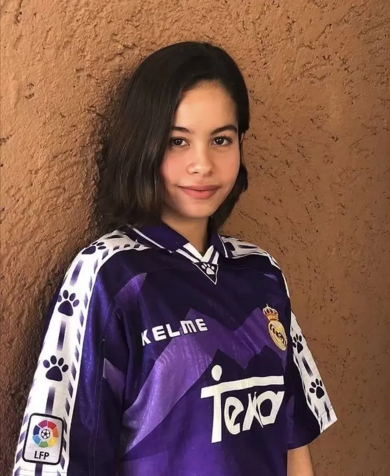 Gái xinh diện áo bóng đá màu tím Kelme tạo dáng tự nhiên trước nền tường nâu Gái xinh diện áo bóng đá màu tím Kelme tạo dáng tự nhiên trước nền tường nâu